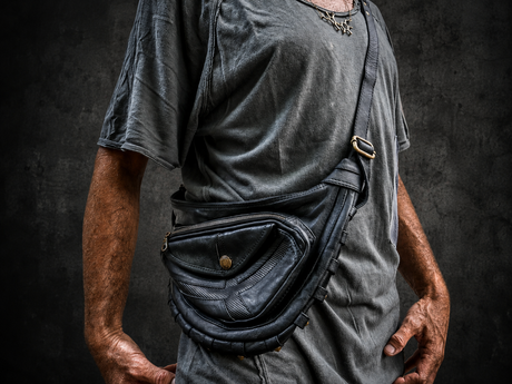 Black Arc Leather Sling Bag by Rebel Armada, black leather crossbody sling with curved body shape, front pockets, brass hardware, adjustable strap, and dark studio background.