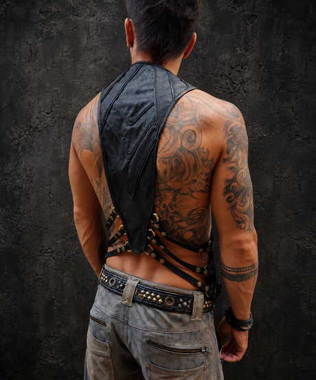 Male model wearing The Black Harness Vest from the back, showing the sculpted leather back panel, adjustable straps, brass hardware, and black leather utility construction.