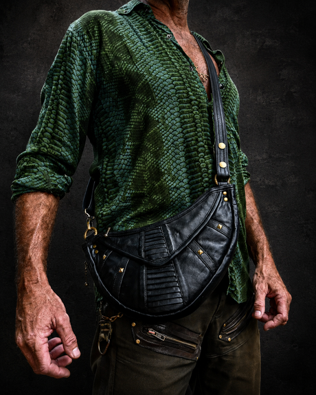 Male model wearing The Black Twin Orbit Harness Bag as a crossbody leather utility pouch against a dark wall background.