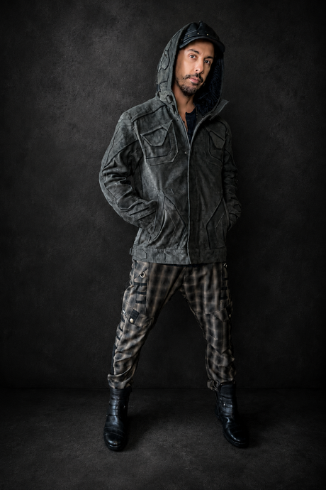 Man wearing the Fabric Sentinel Hooded Jacket in dark olive patterned fabric against a dark studio wall.