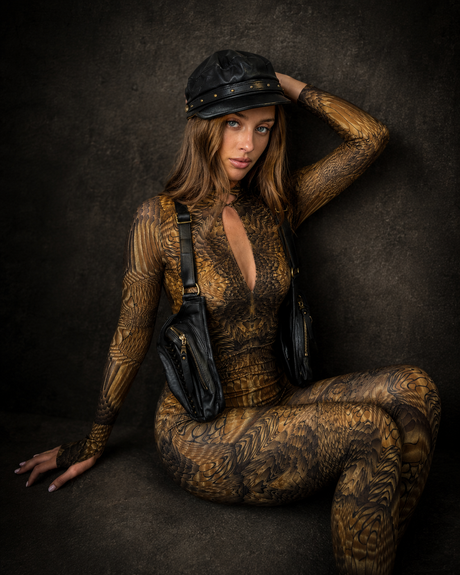 Female model wearing The Black Captain Cap against a dark textured wall, showing the black leather crown, studded front band, and Rebel Armada styling.