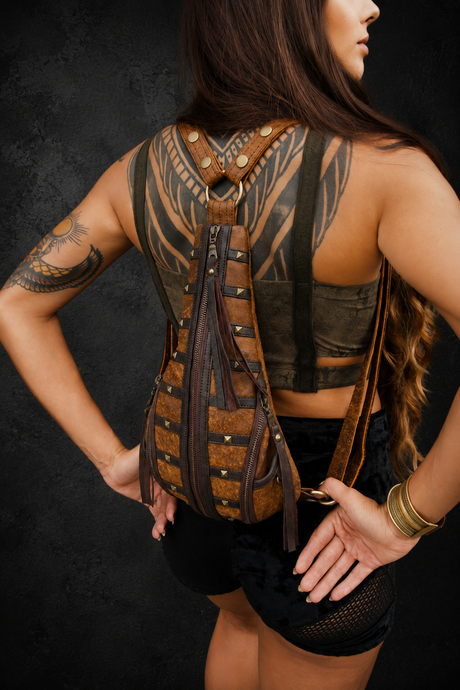 Female model wearing The Bronze Nomad brown leather mini backpack from the back against a dark textured wall.