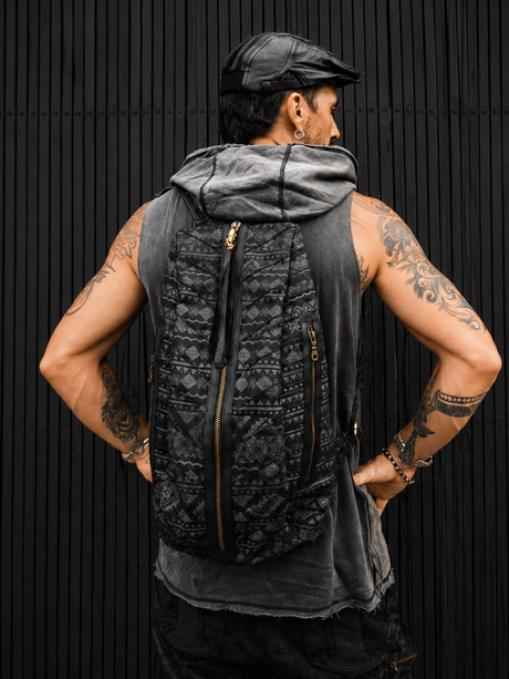 Back view of The Nomad Zip Pack backpack on a model against a black wood wall, showing the geometric grey pattern